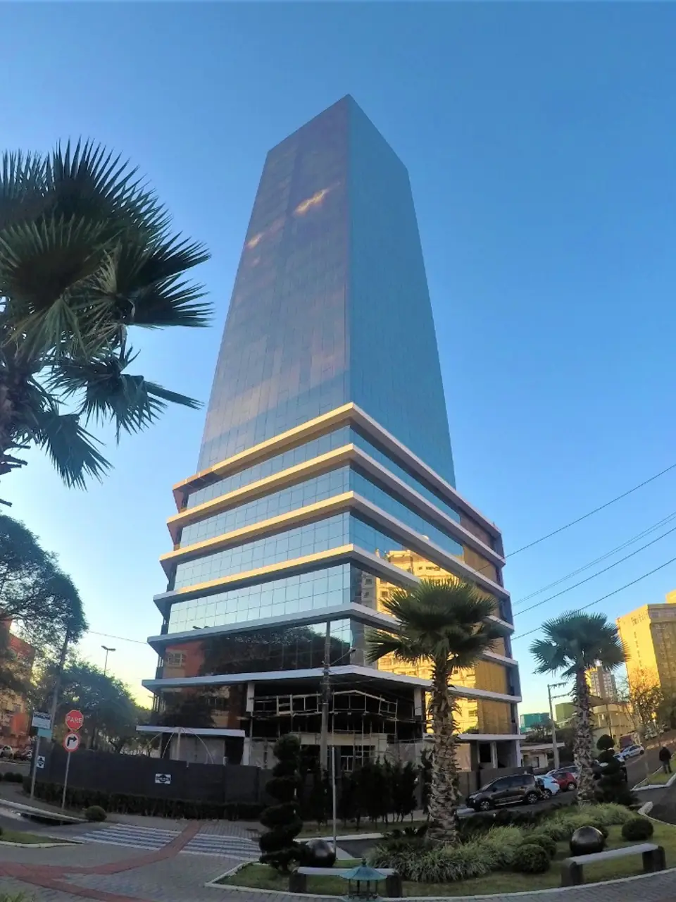 Edifício Il Centenário visto da rua, torre espelhada entre palmeiras no Centro de Chapecó.