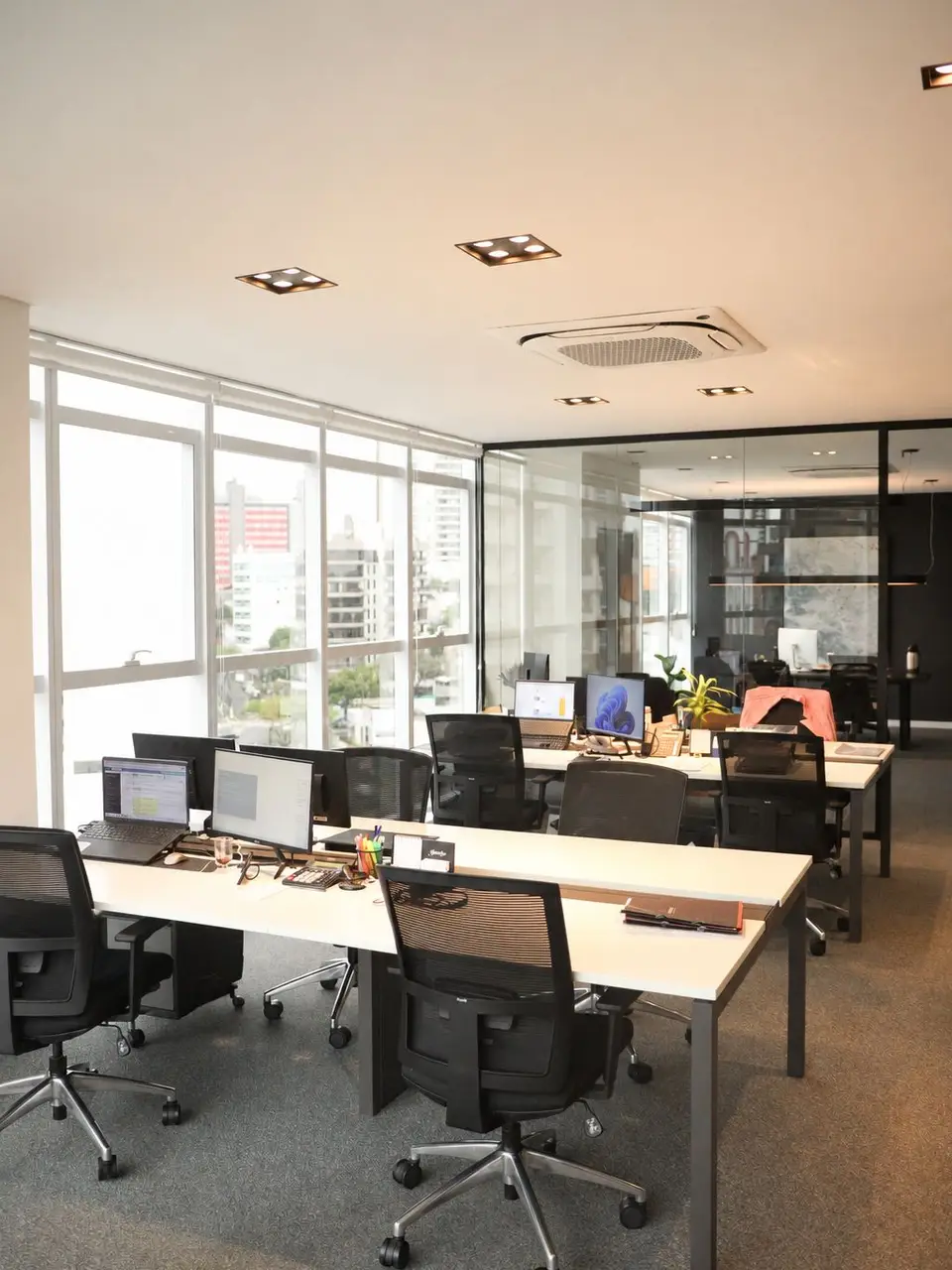 Sala corporativa da equipe, com estações de trabalho, janelas amplas e vista para a cidade.